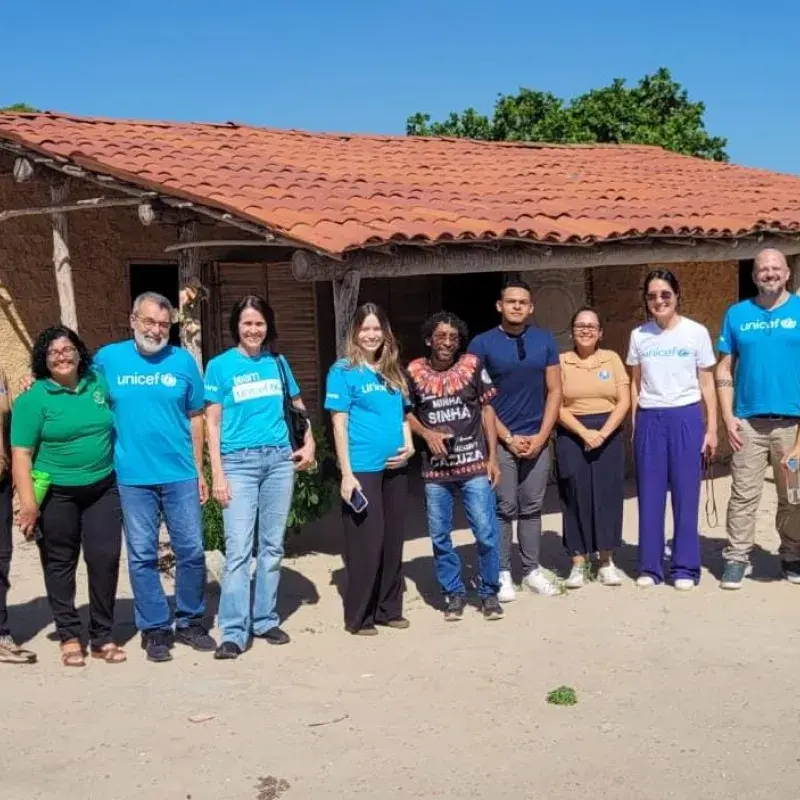 Grupo do UNICEF pousa para foto na frente de uma casa de barro