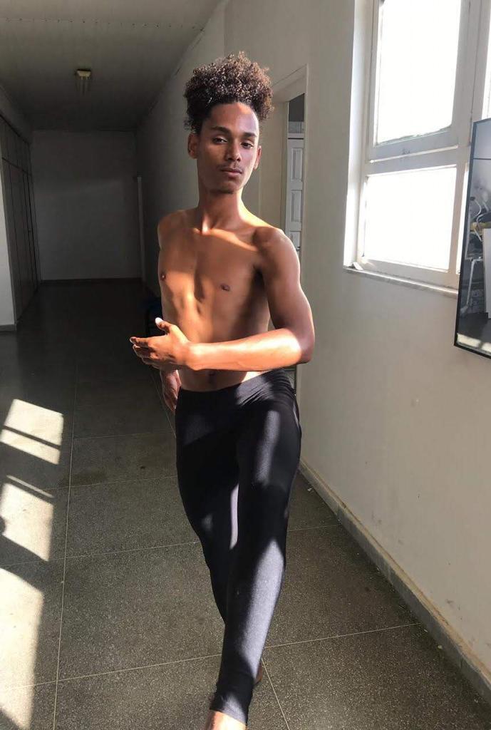 Jovem vestindo uma calça preta e sem camisa posa para câmera em pose de balé