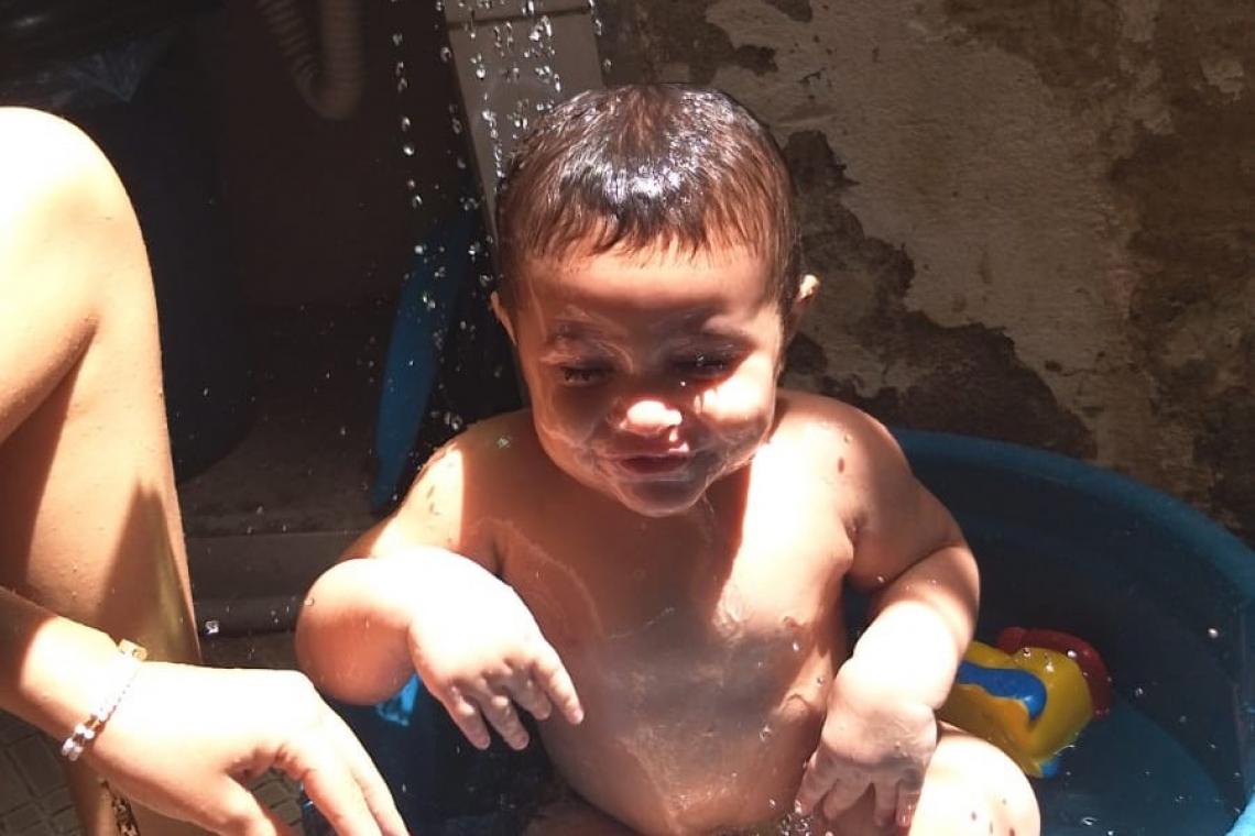 Um bebê aparece sorrindo enquanto toma banho em uma bacia