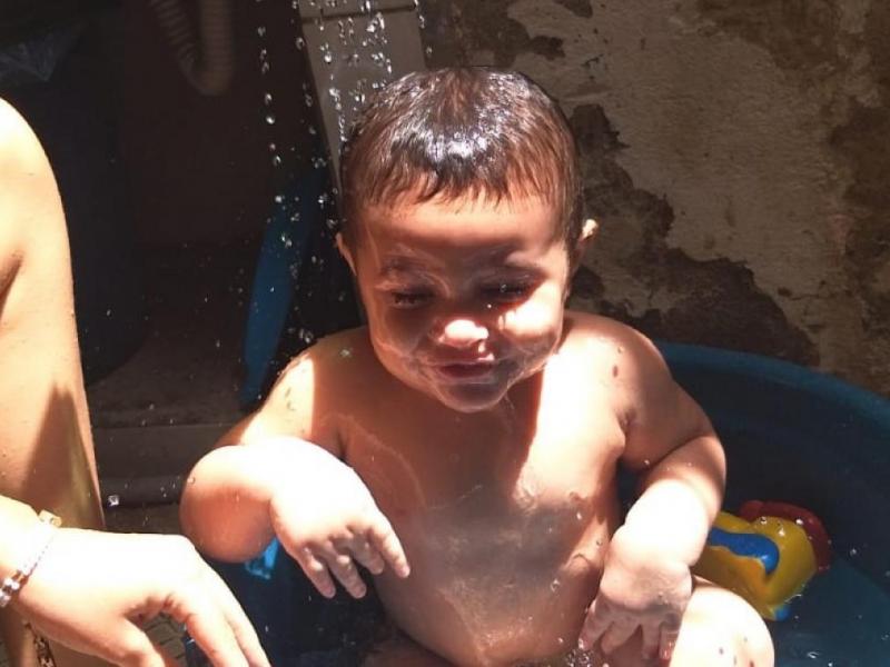 Um bebê aparece sorrindo enquanto toma banho em uma bacia