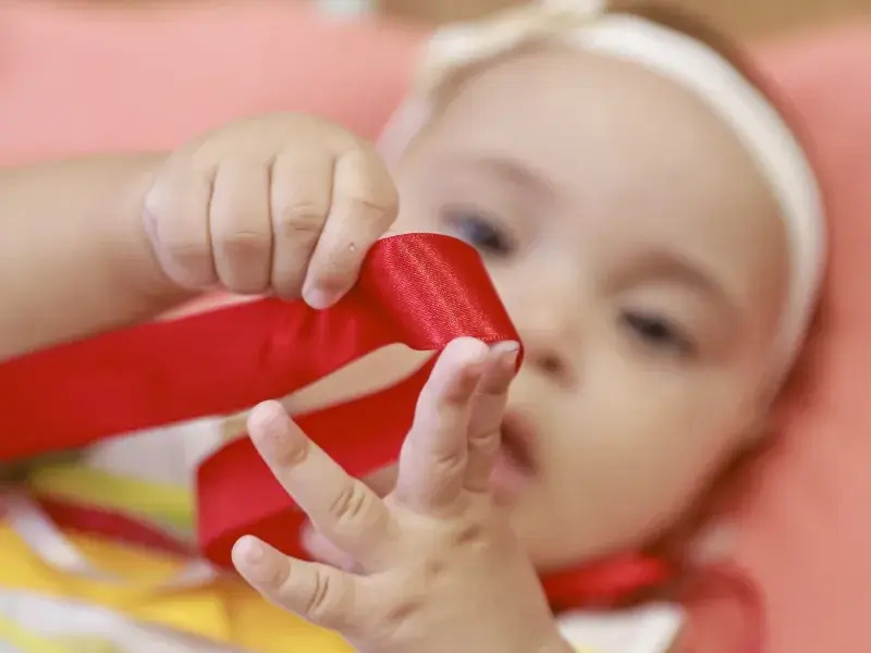 Bebê brinca com laço de fita vermelho
