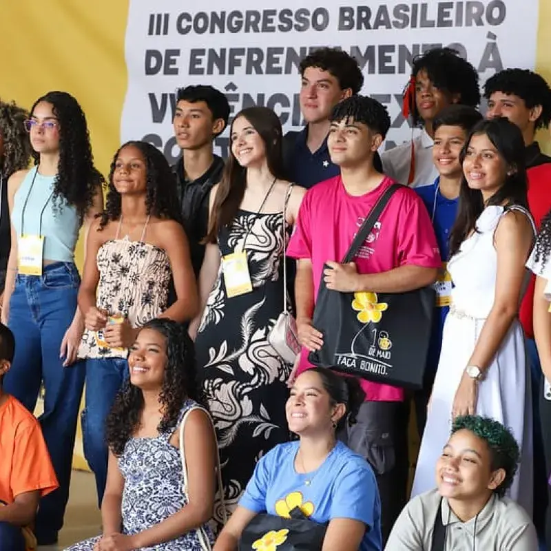 Grupo de adolescentes possam para foto ao fundo banner do evento